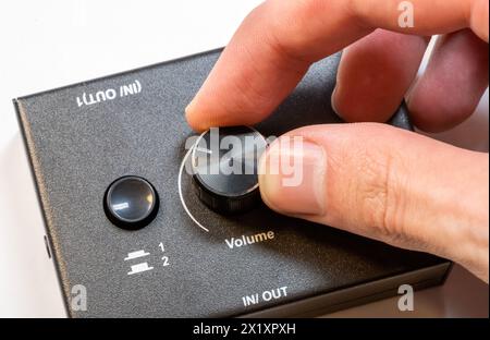 Vue rapprochée d'une main d'homme tournant vers le haut en réglant le bouton de volume sur un appareil audio moderne. Rendre la sortie audio plus silencieuse ou plus forte concept simple, un Banque D'Images