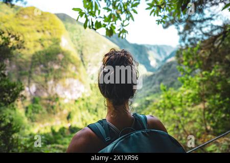 Description : le toursit féminin bénéficie d'une vue panoramique depuis le sentier de randonnée du canal aquatique à une falaise abrupte à travers la forêt tropicale de Madère. Levada de Caldeirão Verde, M Banque D'Images