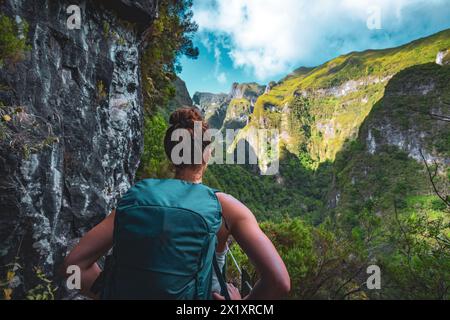 Description : toursit routard féminin jouit d'une vue panoramique depuis le dessous d'un grand mur rocheux le long du canal d'eau à la falaise abrupte à travers la forêt tropicale de Madère. Banque D'Images