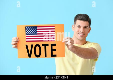 Jeune homme tenant l'affiche avec le VOTE DE mot et le drapeau des États-Unis sur fond bleu clair Banque D'Images