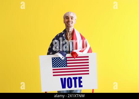 Homme tatoué tenant l'affiche avec le mot VOTE et drapeau USA sur fond jaune Banque D'Images