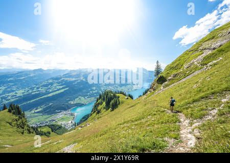 Description : femme athlétique randonne sur un sentier fleuri sur une prairie escarpée avec vue panoramique sur le lac Walensee et les alpes suisses. Schnürliweg, Walensee, composé Banque D'Images