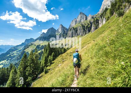 Description : femme sportive marche sur un sentier de randonnée pittoresque entre prairie et arbres et la chaîne de montagnes Churfürsten en arrière-plan. Schnürliweg, Wal Banque D'Images