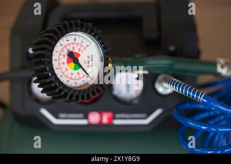 Manomètre analogique avec compresseur vert et tuyau en spirale bleu en arrière-plan. Banque D'Images
