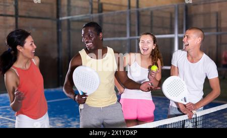 Quatre hommes et femmes souriants avec des raquettes de padel posant sur le terrain Banque D'Images