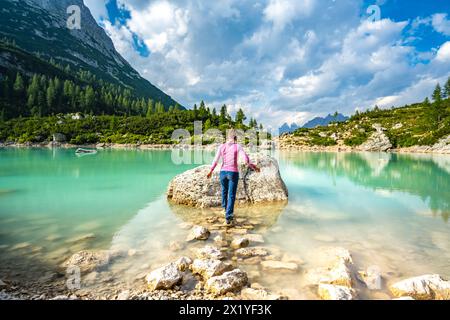 Description : athlétique jeune femme saute sur le chemin de pierre à grand rocher au beau lac turquoise Sorapis dans l'après-midi. Lac Sorapis, Dolomites, BE Banque D'Images