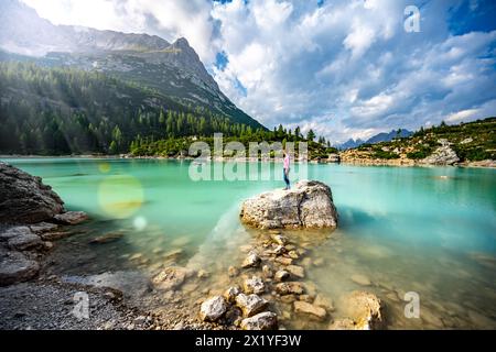 Description : jeune femme athlétique jouit d'une vue depuis un grand rocher sur le magnifique lac turquoise Sorapis dans l'après-midi. Lac Sorapis, Dolomites, Belluno, Banque D'Images