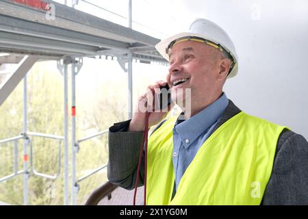 constructeur âgé expérimenté, chef d'équipe de construction, ingénieur de construction dans la protection de casque parlant au téléphone sur le chantier de construction pour le bâtiment re Banque D'Images