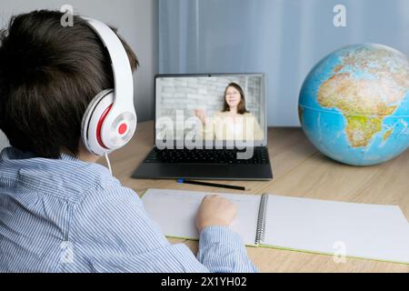 Écolier, enfant de 7-8 ans faisant ses devoirs devant un ordinateur portable, le professeur à l'écran mène une leçon sur Internet, conférence en ligne, le c Banque D'Images