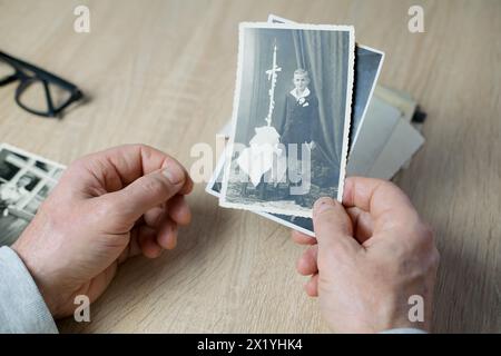 main masculine tenant de vieilles photographies monochromes vintage d'enfants 1940 - 1950 en couleur sépia sont dispersées sur une table en bois, concept de généalogie, memor Banque D'Images