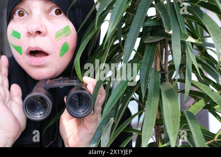 gros plan curieuse femme islamique dans la peinture de guerre, tenant des jumelles de champ avec zoom, regardant depuis les buissons, espionnant le mari infidèle, les voisins, les obs Banque D'Images