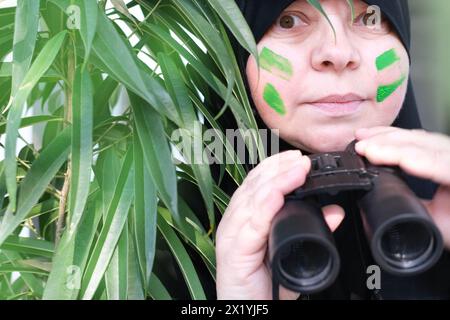 gros plan curieuse femme islamique dans la peinture de guerre, tenant des jumelles de champ avec zoom, regardant depuis les buissons, espionnant le mari infidèle, les voisins, les obs Banque D'Images