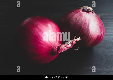 Paire d'oignons rouges entiers sur un fond de bois foncé : photo de style vintage d'un groupe de deux oignons espagnols violets sur une table en bois foncé Banque D'Images