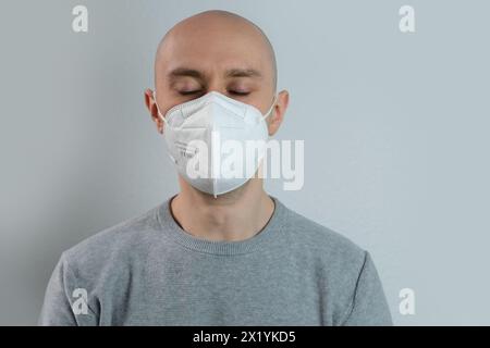 Gros plan du visage jeune homme en masque blanc, respirateur de protection avec haut degré de protection de classe FFP2, coronavirus COVID-19 en europe, a fermé le sien Banque D'Images