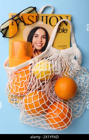 Sac à ficelle avec magazine, fruits et accessoires d'été sur fond bleu clair, pose plate Banque D'Images