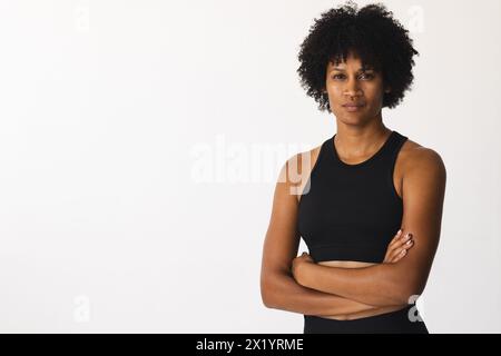 Instructeur de yoga féminin biracial debout dans le studio avec les bras croisés, regardant sérieux, espace de copie Banque D'Images