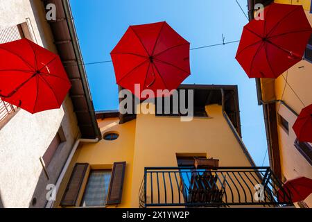 Rue de la ville à Porto Ceresio avec parapluies suspendus dans une journée d'été ensoleillée à Porto Ceresio, Lombardie, Italie. Banque D'Images