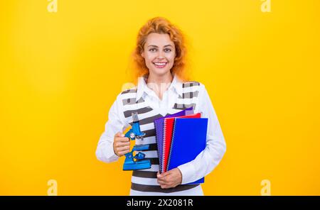 Professeur avec microscope sur jaune. Sciences biologiques pour la femme. La recherche microscopique. Une femme professeur de biologie scolaire tient un microscope. Femme enseignante de Banque D'Images