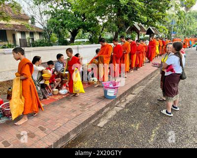 Luang Prabang, Laos. 16 avril 2024. Les moines et les novices défilent dans les rues de Luang Prabang dans leurs robes orange tôt le matin et reçoivent de la nourriture comme du riz collant et des fruits des habitants. La ronde de l'aumône est un rituel ancien. Le spectacle fascinant attire maintenant de plus en plus de touristes du monde entier. Crédit : Carola Frentzen/dpa/Alamy Live News Banque D'Images