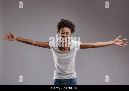 Jeune femme aux yeux vifs offre un geste accueillant, sa tenue suggérant confort et simplicité Banque D'Images