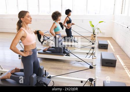 Trois femmes diverses font de l'exercice sur des machines de reformage pilates dans un studio Banque D'Images