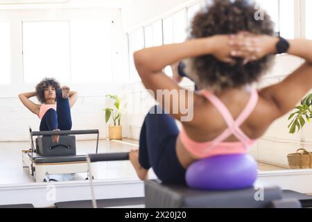 Jeune femme biraciale portant un haut rose s'exerce sur un reformeur Pilates en studio, espace copie Banque D'Images