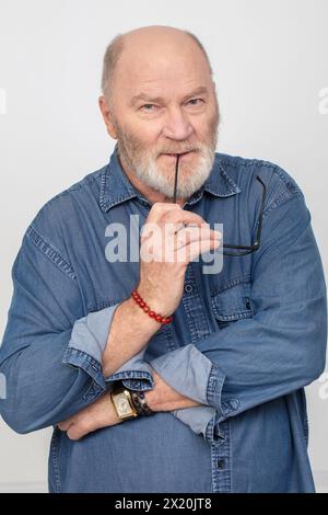 Portrait d'un homme aux cheveux gris attrayant dans une chemise en denim isolé sur un fond gris. Grand-père barbu de type européen. Banque D'Images
