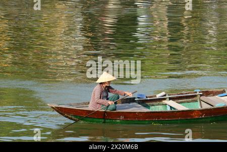 Une vietnamienne ramant transportant des marchandises ou des personnes à travers la rivière Thu bon à Hội an, Vietnam. Banque D'Images