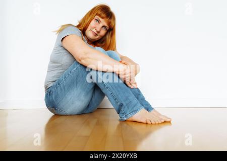 Portrait pleine longueur magnifique femme joyeuse assise sur parquet, espace vide un appartement sans meubles Banque D'Images