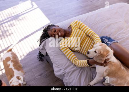 Jeune femme afro-américaine allongée sur le sol à l'intérieur à la maison, caressant un chien, copiez l'espace Banque D'Images