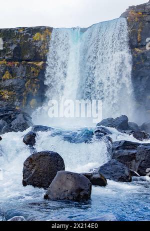 Une cascade avec un gros rocher devant elle. L'eau coule le long de la roche et les roches sont dispersées autour de la cascade. La scène est sereine Banque D'Images