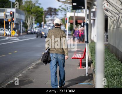 Homme marchant à l'arrêt de bus dans une rue de banlieue animée. Des gens méconnaissables marchant sur le trottoir piétonnier. Auckland. Banque D'Images