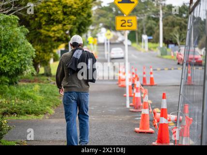 Homme marchant sur un sentier piéton. Cônes orange et clôtures métalliques sur la route. Travaux routiers à Auckland. Banque D'Images