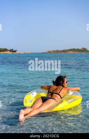 Vue arrière d'une femme sur un oreiller gonflable beignet sur l'eau turquoise Banque D'Images