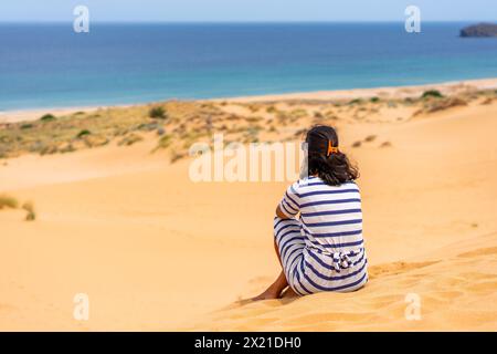 Vue arrière d'une femme au sommet d'une dune de sable regardant la mer Banque D'Images