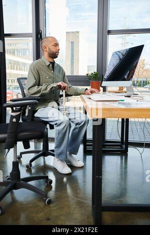 homme afro-américain handicapé avec myasthénie grave dans la tenue d'entreprise se concentre sur un bureau, tapant sur un écran d'ordinateur parmi les fournitures de bureau. Banque D'Images