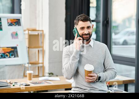 Un homme d'affaires dans un bureau d'entreprise multitâche en parlant sur un téléphone portable tout en tenant une tasse de café. Banque D'Images