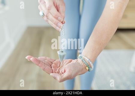 Femme tenant pendule sur la main portant des bracelets en cristal et bague Banque D'Images