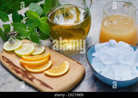 Thé glacé maison à base de tisane avec jus de pomme, jus d'orange, menthe à l'eau, marjolaine sauvage, étape 3 : tranches d'orange, tranches de citron et glace sont adde Banque D'Images
