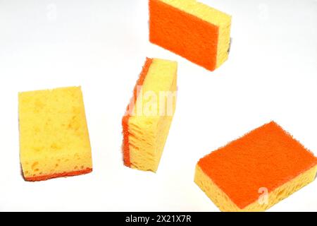 Plusieurs éponges à vaisselle orange reposent aléatoirement sur un fond blanc. Banque D'Images