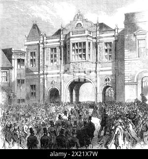 Ouverture de la nouvelle Bourse de maïs à Aylesbury, 1865. La cérémonie d'ouverture de la nouvelle Bourse de maïs et du marché dans la ville prospère d'Aylesbury a eu lieu mercredi - le très honorable Lord Carington, Lord Lieutenant de Buckinghamshire, présidant... le site de la nouvelle Bourse de maïs est dans l'ancienne place du marché... l'édifice, conçu par M.R. D. Brandon, de Berkeley-Square, est du style élisabéthain de l'architecture ; les matériaux sont en briques rouges, avec des parements de pierre. La façade, attenante au County Hall, se compose de trois arcades - une pour les voitures, les deux autres pour les passagers à pied Banque D'Images