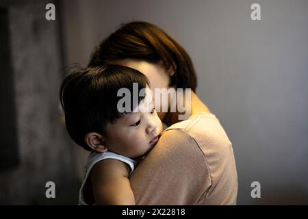Mère porte l'enfant dans ses bras. Le petit garçon est allongé sur l'épaule de sa mère. Un fils triste embrasse maman. Banque D'Images