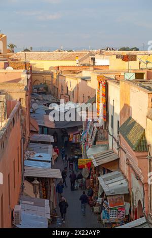 Marrakech, Maroc - 16 janvier 2019 : Souk dans une rue narow de la Médina avec les montagnes de l'Atlas derrière. Banque D'Images