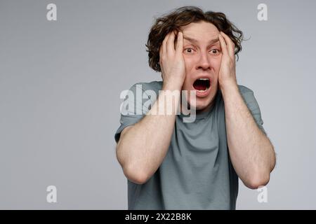 Portrait de studio de taille vers le haut du jeune acteur caucasien démontrant un sentiment de terreur, fond gris, espace de copie Banque D'Images