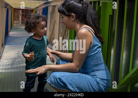 Maman s'accroupit pour discuter avec son fils alors qu'ils s'arrêtaient sur une passerelle colorée en Amérique latine. Concept de maternité et fête des mères. Banque D'Images