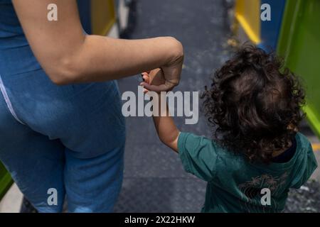 Maman et son fils latino-américain avec le dos tourné marchent main dans la main dans quelques escaliers sur la passerelle. Concept de maternité et de fête des mères. Banque D'Images