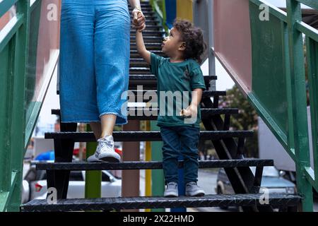Maman et fils latino-américains marchent main dans la main dans une volée d'escaliers sur la passerelle. Concept de maternité et de fête des mères. Banque D'Images