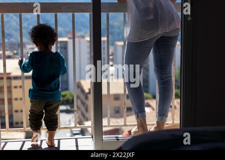 Maman latino-américaine (30 ans) et son fils (2 ans), debout sur le balcon, donnent sur la ville du haut de leur appartement. Concept de fête des mères, célibataire Banque D'Images