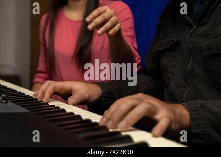 Professeur latino-américain méconnaissable enseigne et corrige la posture pour jouer du clavier de piano. Concept de leçons de musique Banque D'Images