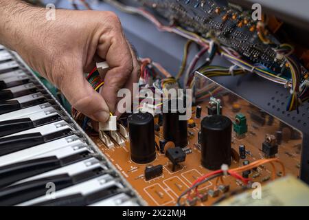 Un technicien en électronique latino-américain répare un piano dans le centre de service. Réparation de concept, musique, électronique Banque D'Images